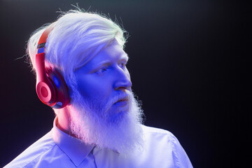 An old albino grandfather listening to music with new, red headphones, looking serious, isolated on a colorful background.