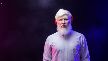 An old albino grandfather listening to music with new, red headphones, looking serious, isolated on a beautiful background.