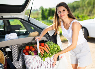Portrait of young female amateur gardener with freshly picked vegetables standing near car