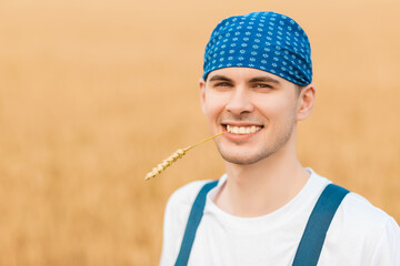 Farmer smiling in the camera while holding a wheat ear in his month.