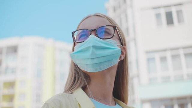 Portrait young woman with glasses looking around with medical mask being outdoors during quarantine pandemic covid-19 close up slow motion