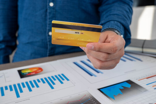 The businessman stands the yellow credit card ahead as he sits at the office desk.