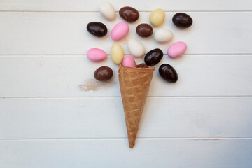 Top view of ice cream cone with sweet almond eggs on white wooden table