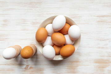 Free-range organic brown and white eggs in bowl and boiled eggs in holders on vintage wooden background