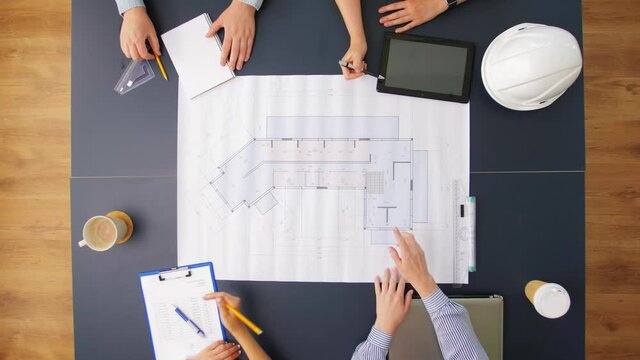 construction business, architecture and team work concept - team of architects with blueprint, gadgets and papers working at office table