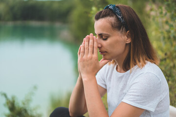 Fototapeta premium Woman closed her eyes, praying in outdoors. Hands folded in prayer concept for faith, spirituality and religion. Peace, hope, dreams concept