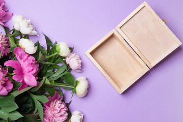 Obraz na płótnie Canvas bouquet of pink and white peony and opened wooden box on purple colored paper background