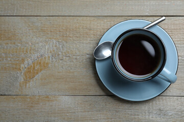 Cup of aromatic black tea and spoon on wooden table, top view. Space for text