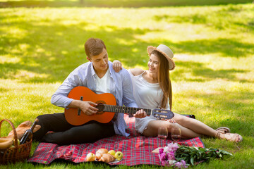 Affectionate young man playing guitar for his girl on romantic date in park