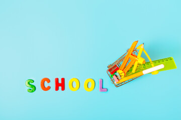 School supplies in shopping cart and the word school of multicolored letters on a blue background. Concept back to school. Concept for a store of stationery for school. copy space, top view.