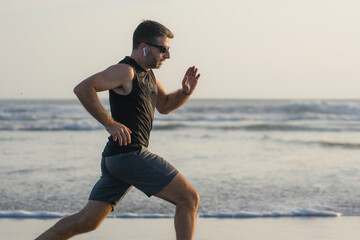 jogging Summer workout - young attractive and fit runner man training on beautiful beach running barefoot free and happy by the sea in fitness and healthy lifestyle concept