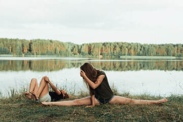 two girls do gymnastic exercises outdoor in a picturesque place by the river and having fun