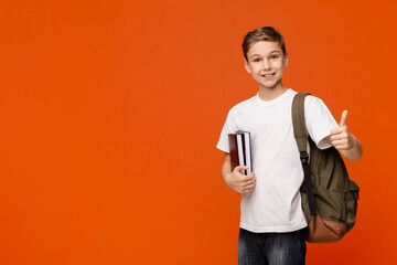 Cheerful teen boy with backpack and books gesturing thumb up