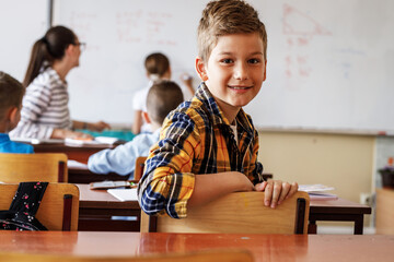 Portrait of young boy in primary school classroom.He sitting at the desk and looking at camera.	
