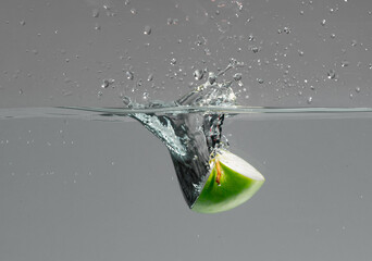 Green apple slice falls into water and creates beautiful air bubbles and water splashes
