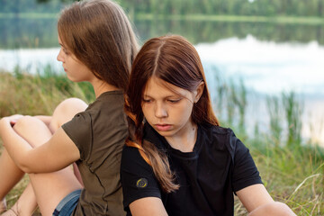 Fototapeta premium two teenage girls are braided in one braid on a picturesque river bank, the concept of friendship and the ability to find a compromise