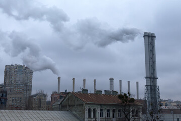 Smoke comes from industrial chimneys above the rooftops. The sky is covered with gray clouds....
