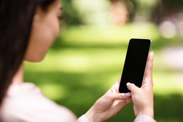 Woman using smartphone with blank black screen outdoors, mockup