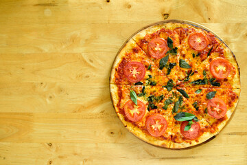Homemade pizza with cheese and tomatoes and basil on a wooden table with copy space.
