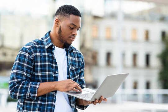 Black man using laptop, standing in city