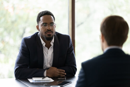 Two business partners meet in office solve current issues. Caucasian applicant rear view answer questions while African serious hr manager listen him feels sceptic. Negotiations, job interview concept