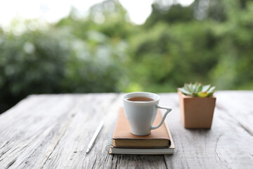 White teacup with leather book and silver pencil and small succulent plant on wooden table