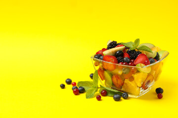 Bowl of fresh fruit salad on yellow background, space for text