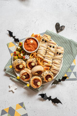 Scary sausage mummies in dough with funny eyes on table. Halloween food. Top view. Flat lay