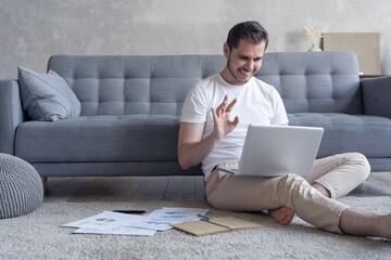 Man working on laptop computer sitting on the floor with his diary and official papers at home.