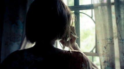 Silhouette of a woman receiving a grim call while facing the window at home. Distress, loss, or...