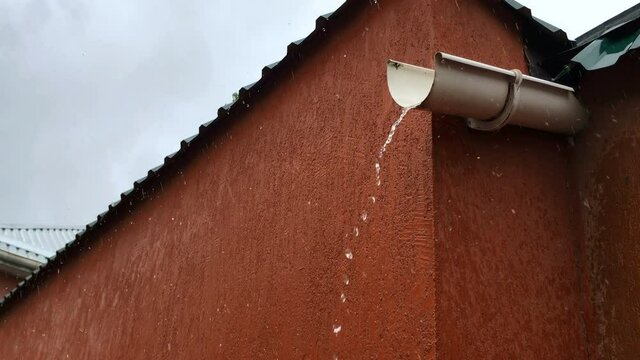 Water flow drips down metal drainpipe during the rain. Close-up.