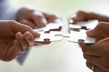 Close up hands of four businesspeople hold pieces of white puzzle, assemble jigsaw, put it...