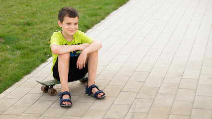 A boy of European appearance sits on a skateboard on a summer day