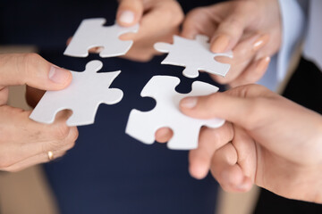 Close up hands of associates four teammates holding white pieces of puzzles, people search and find...