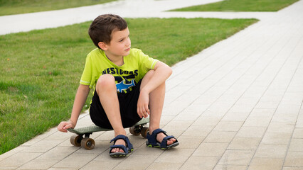 A boy of European appearance sits on a skateboard on a summer day © Mari