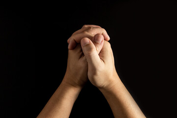 The man's hand that clasped his hand praying has a black or dark background.An expression of wish, hope, belief and faith.