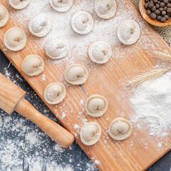 Fototapeta na wymiar Raw dumplings or ravioli on a cutting Board with ingredients for cooking. Recipe of the Russian cuisine, top view