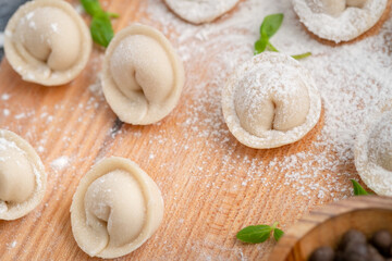 Raw homemade dumplings and a Basil leaf with flour on a wooden Board close-up.