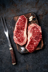 Two raw new York steaks on a chopping Board with meat fork. Wagyu meat for grilling, top view