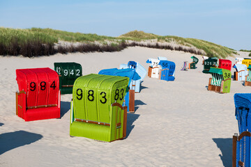 Red, green and blue beach chairs in white sand in the morning on the Frisian island of Juist.