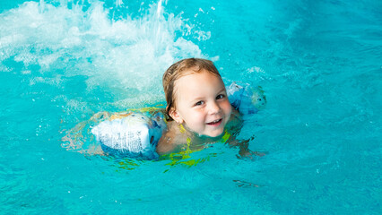 Fototapeta na wymiar Cute girl splashes in the water in the pool in armbands