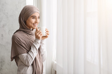 Relaxed Arab Woman In Hijab Enjoying Morning Coffee Near Window At Home