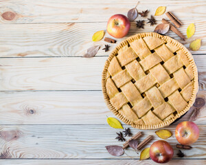 Homemade apple pie with ripe apples, species and autumn leaves on light rustic wooden background,...