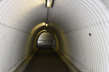 Urban pedestrian subway or underpass below motorway. Passage has corrugated surface of walls in the...