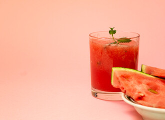 Delicious red watermelon juice with sliced fruit pieces on a plate. A sprig of mint in a glass. Copy space. Summer food concept