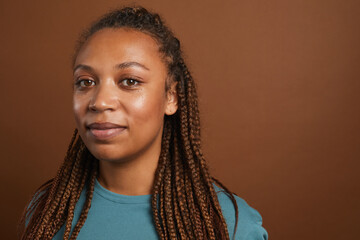 Minimal head and shoulders portrait of modern African-American woman smiling at camera while standing against brown background in studio, copy space