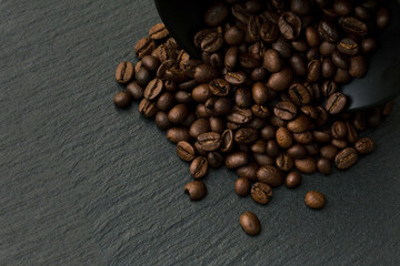 Lots of coffee beans in a Cup on a black textured background of slate stone