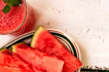Delicious red watermelon juice with sliced fruit pieces on a plate. A sprig of mint in a glass. Copy space. Summer food concept