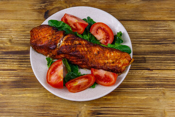 Grilled salmon fillet with spinach and tomatoes on wooden table. Top view