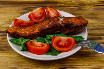 Grilled salmon fillet with spinach and tomatoes on wooden table